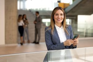 Freundliche Maklerin lehnt sich an eine Brüstung und hat ein Handy in der Hand